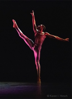 Male African-American dancer bathed in red light with lifted leg